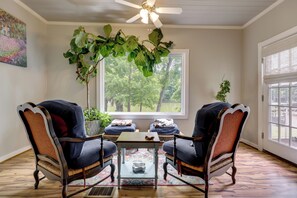 A room with two upholstered chairs, a small table, a ceiling fan, a window with a view of trees, and a plant. - Spacious Lake Placid Retreat w/ Gorgeous Views! (Seguin)