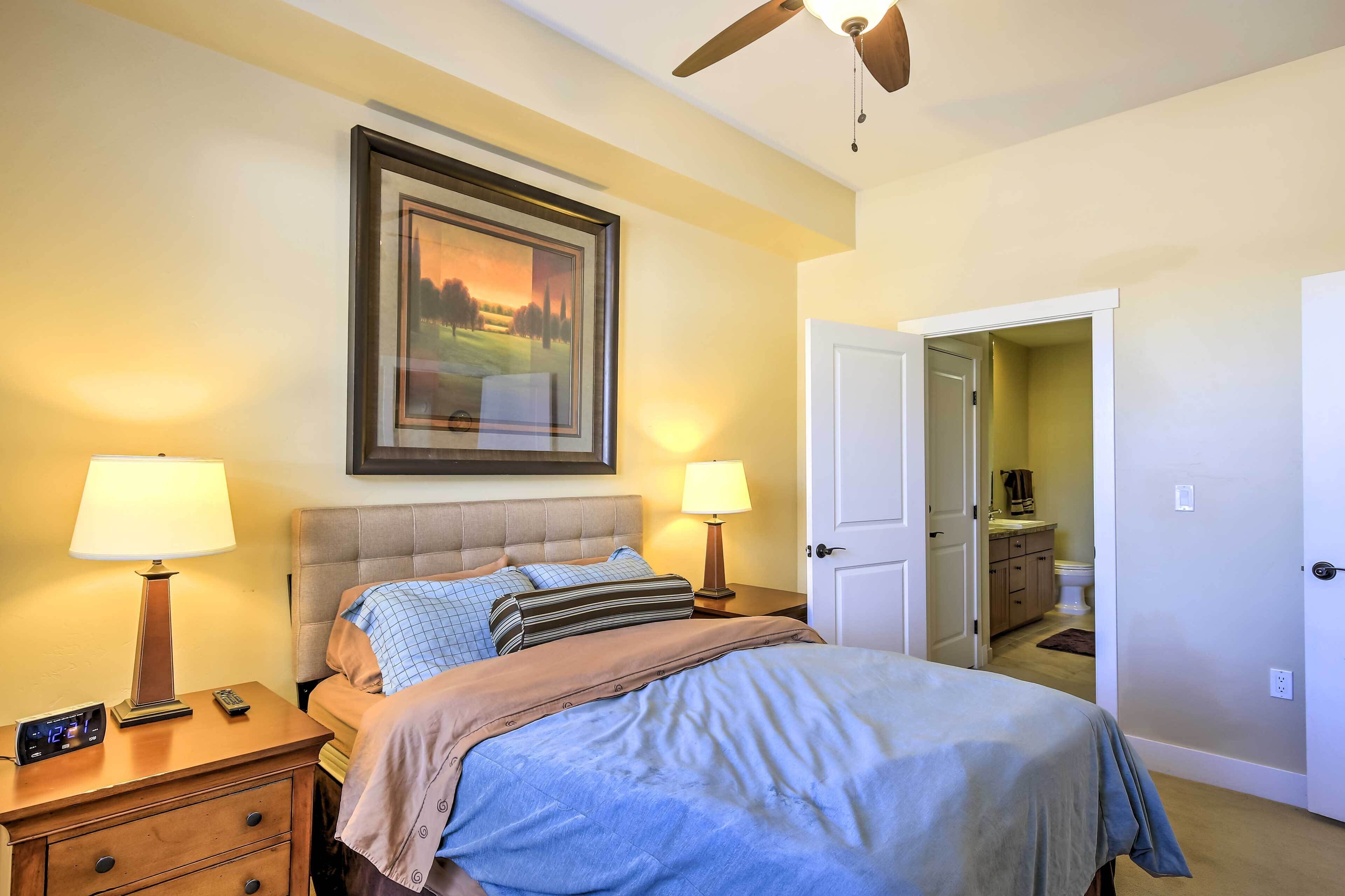 A bedroom with a bed, two bedside tables with lamps, a ceiling fan, and a framed picture on the wall.