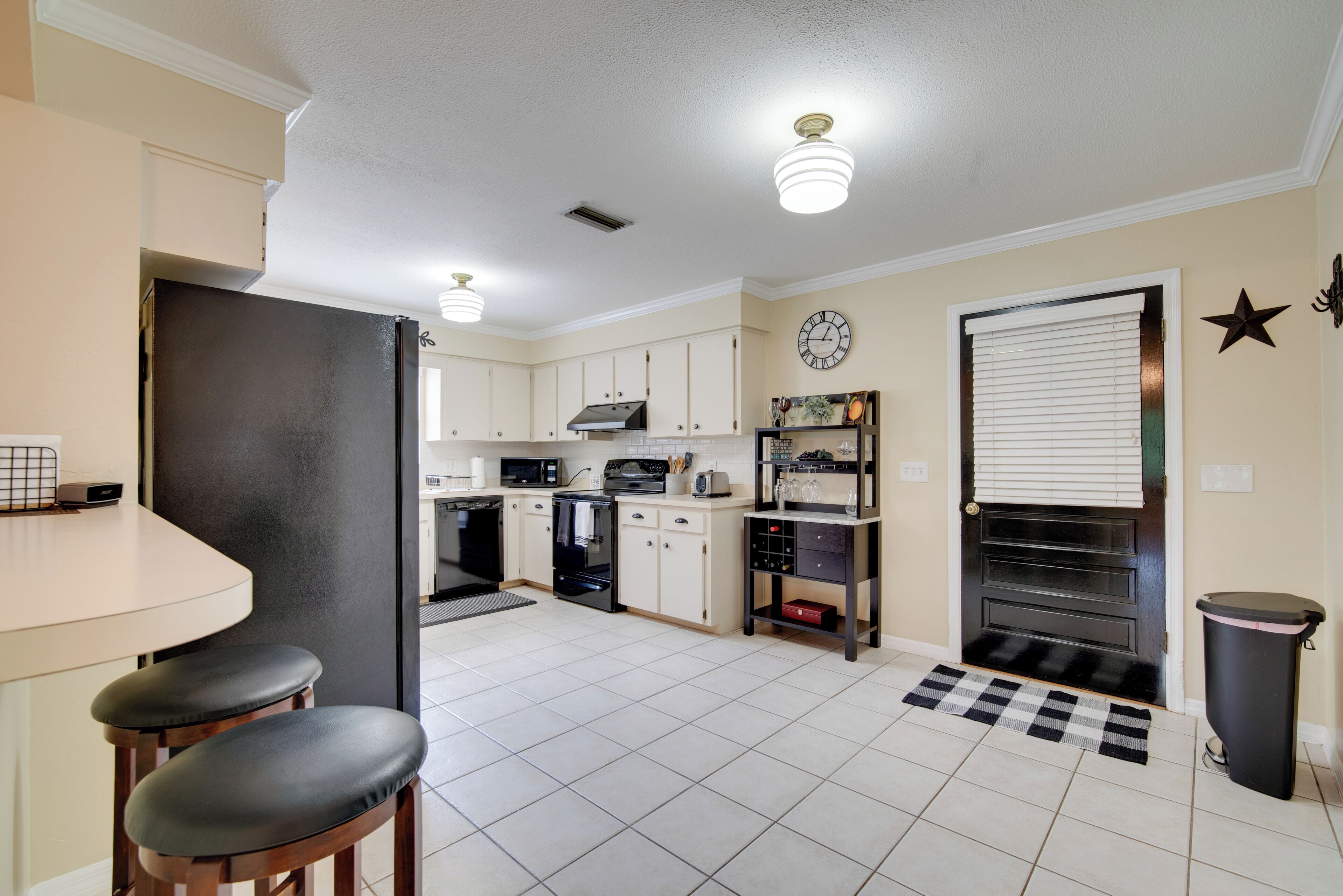 A kitchen with a refrigerator, stove, oven, and sink. There are two stools and a small table.