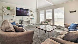 Ett vardagsrum med en platt-TV, en soffa, ett soffbord och ett skrivbord med hyllor.