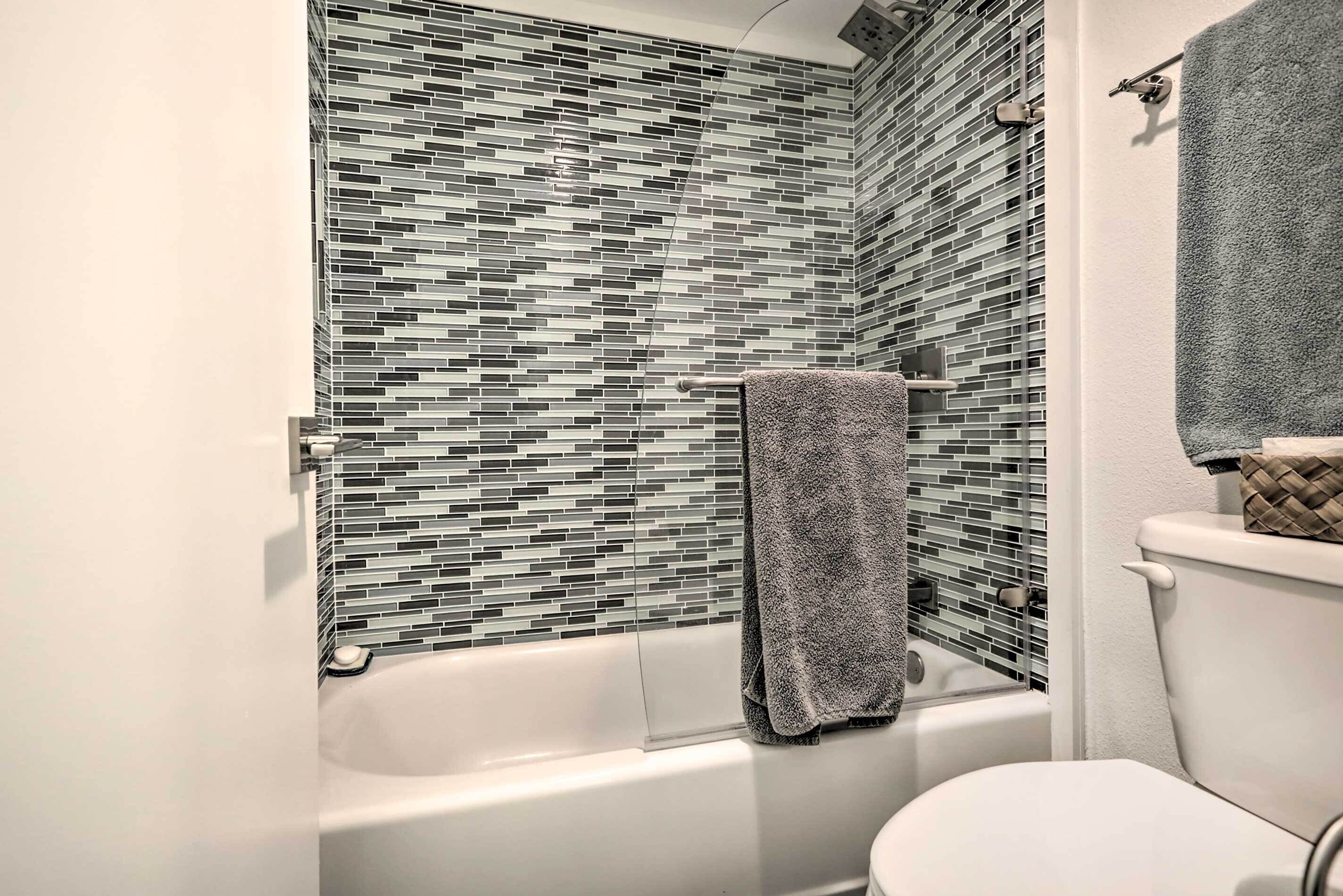 A bathroom with a tiled shower wall, a bathtub, and a toilet.