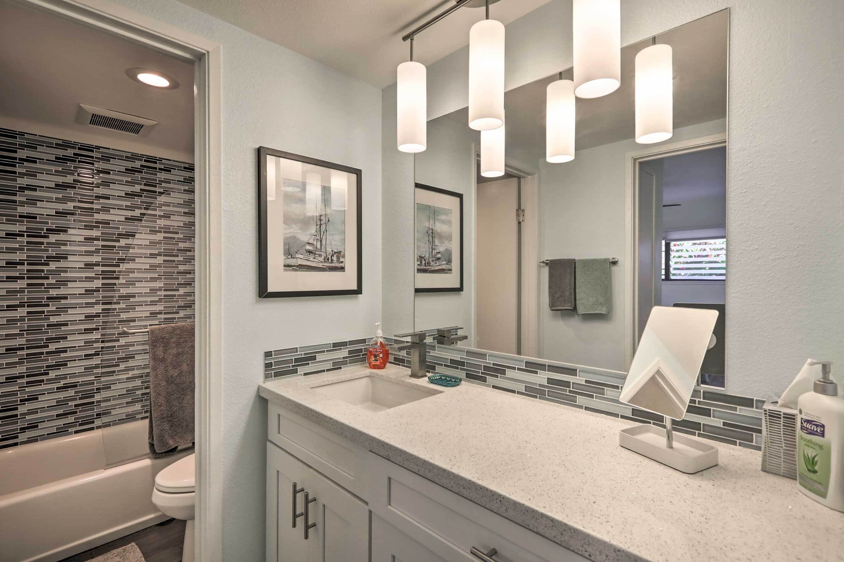 Une salle de bain moderne avec un grand miroir, un lavabo doté d’un distributeur de savon et un porte-serviettes.