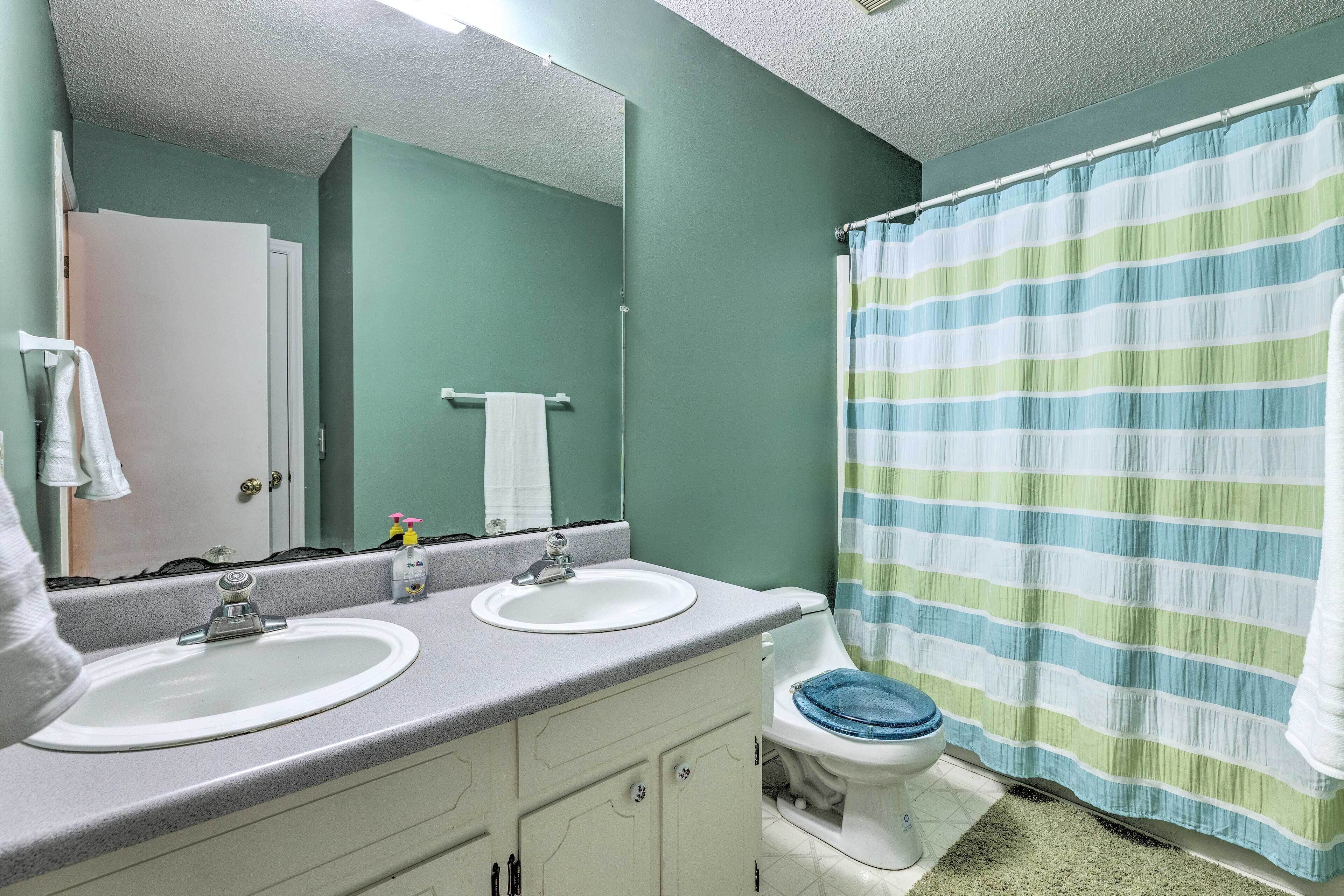 Een badkamer met twee wasbakken, een toilet, een douchegordijn en een spiegel.
