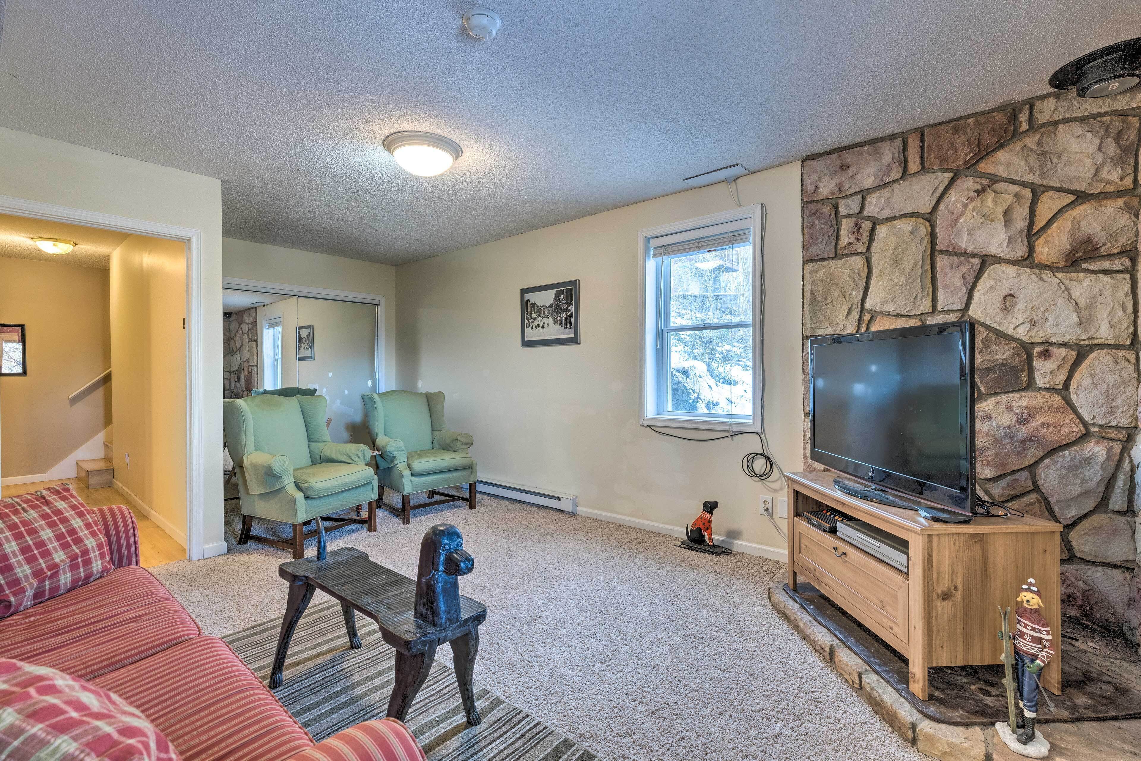 A living room with a stone fireplace, a television, and a staircase leading to another room.