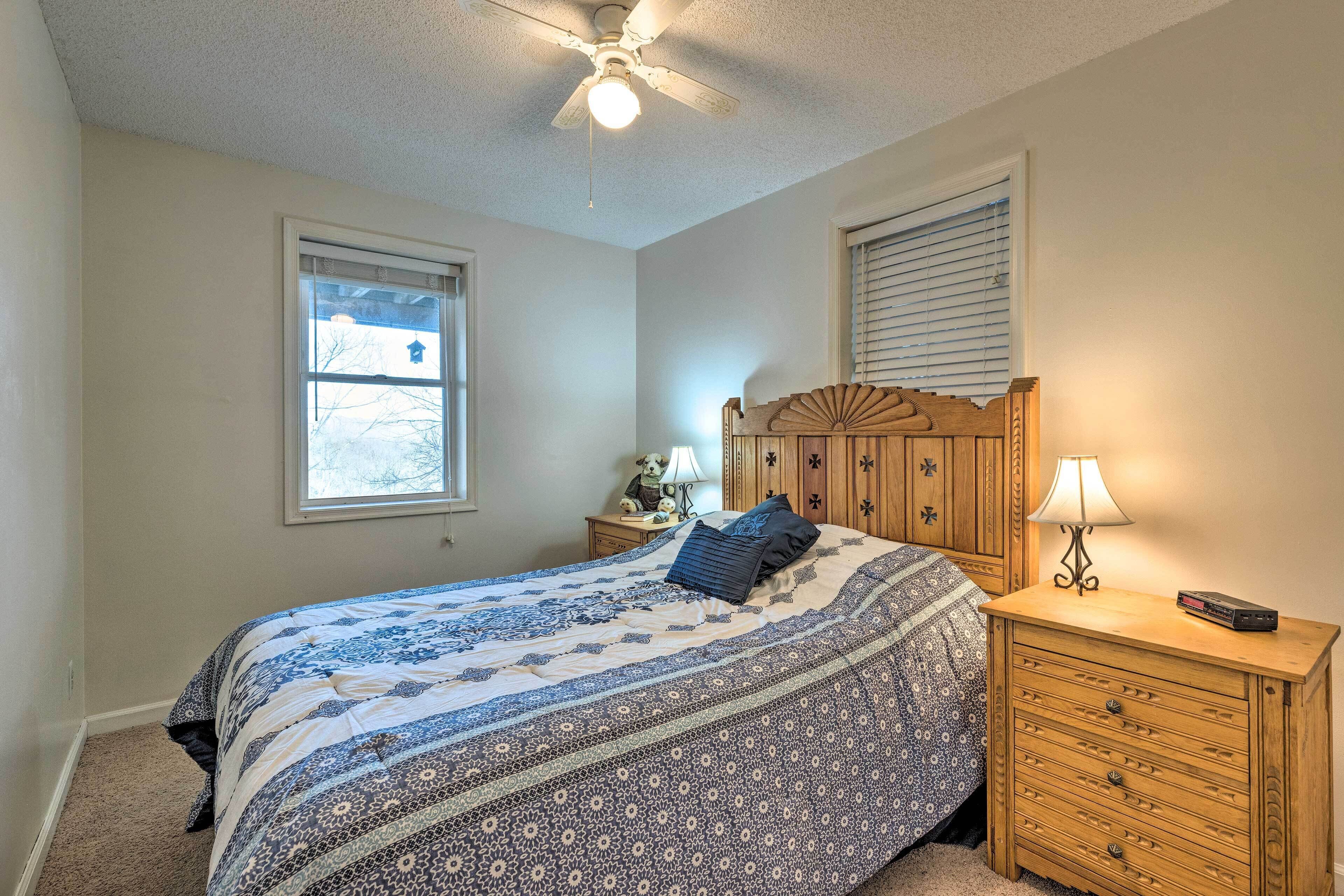 A bedroom with a bed, a nightstand, a dresser, a ceiling fan, and a window.