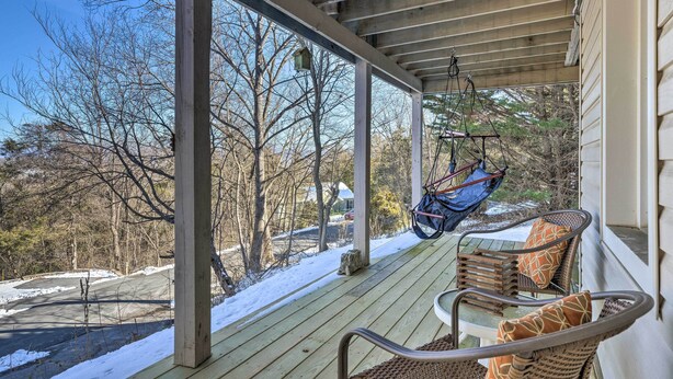 A covered porch with wicker chairs and a hanging chair, overlooking a snowy landscape with trees and a road. - Massanutten Retreat w/ Double Deck & Mtn View! (McGaheysville)