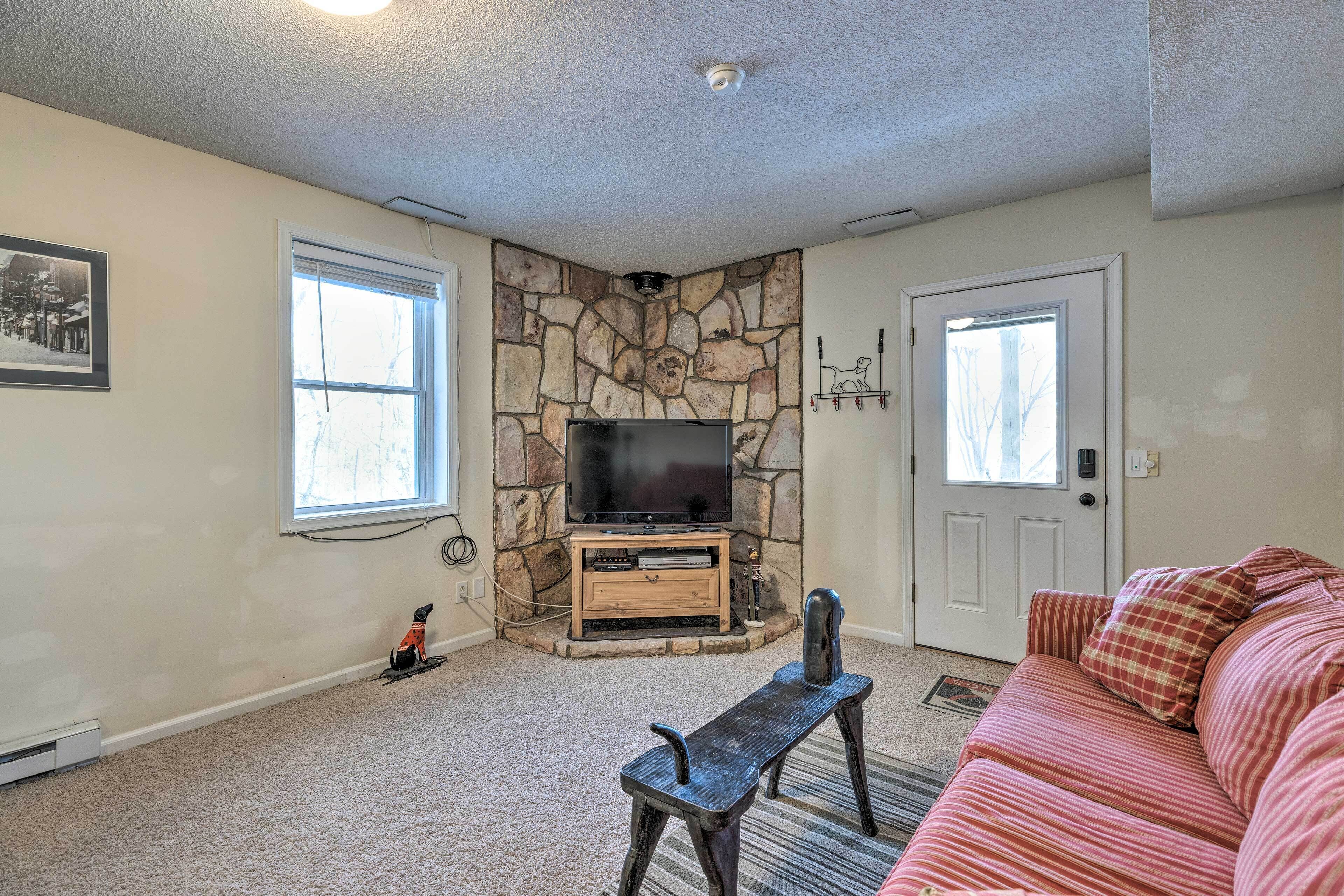 A living room with a stone fireplace, a television on a wooden stand, a red-striped couch, and a door with a window.