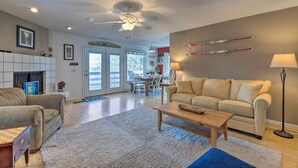 A living room with a beige sofa, a wooden coffee table, a fireplace, and a dining area with a table and chairs. - Massanutten Retreat w/ Double Deck & Mtn View! (McGaheysville)