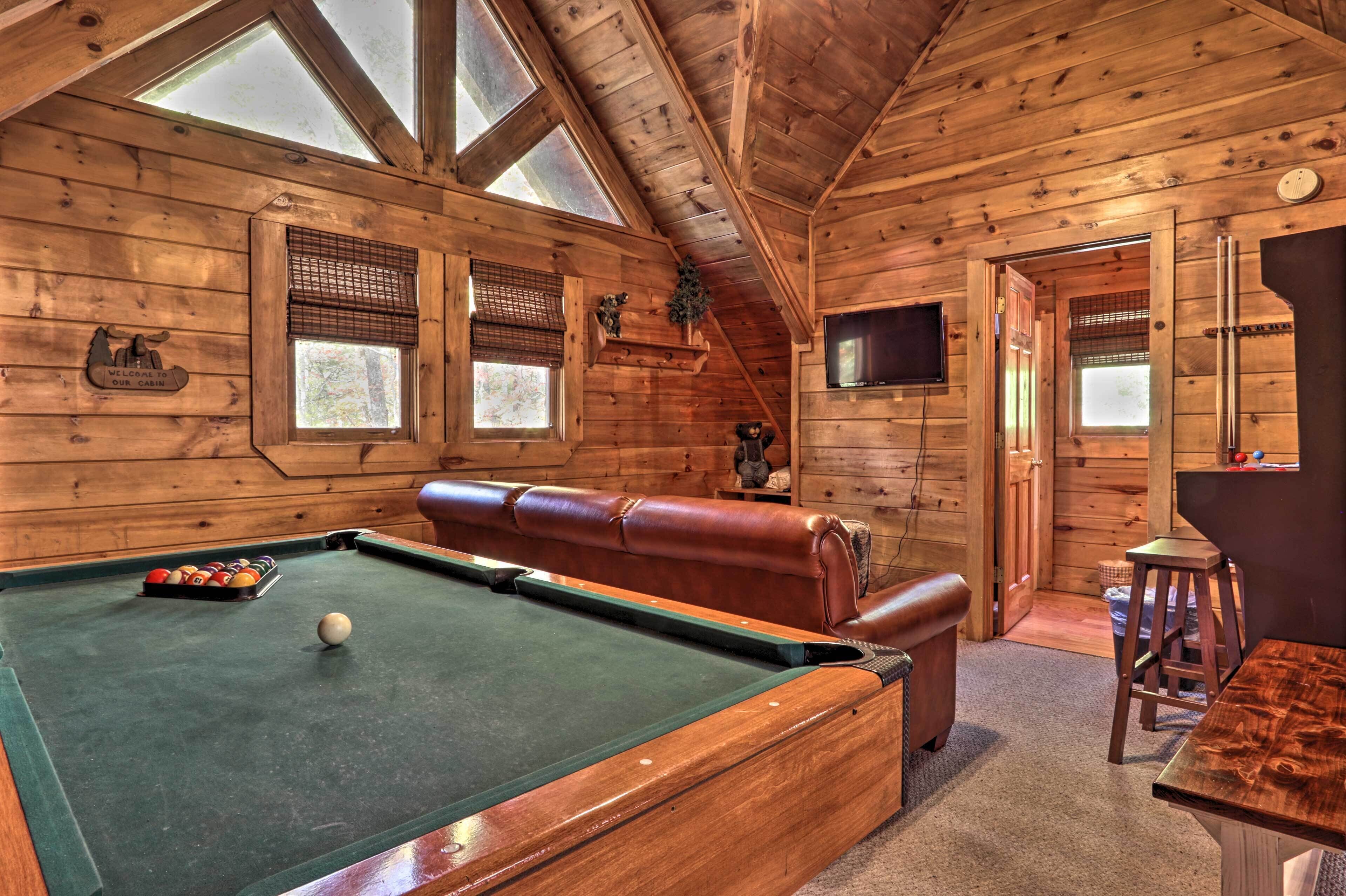 A wooden cabin interior with a pool table, leather sofa, and a television.