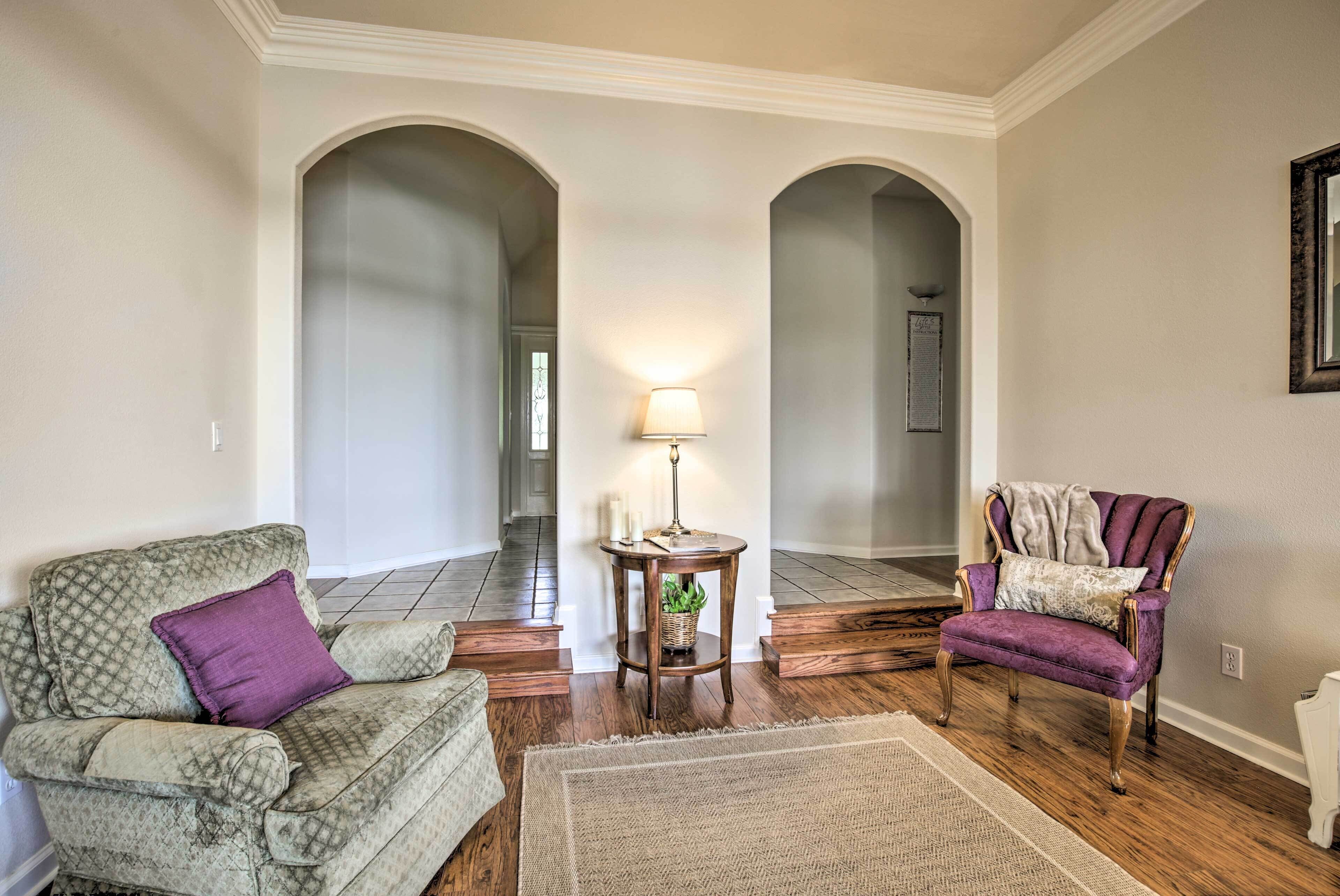 Una sala de estar con un sillón estampado, una silla morada, una mesita con lámpara y una alfombra.