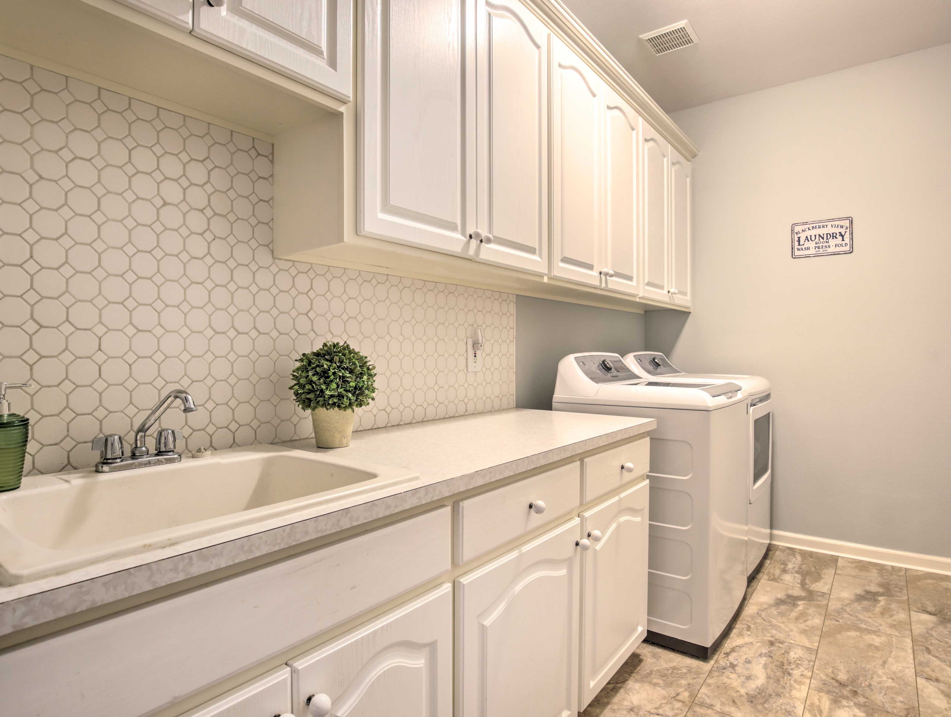 A kitchen with white cabinets, a sink, a plant, and a washer and dryer.