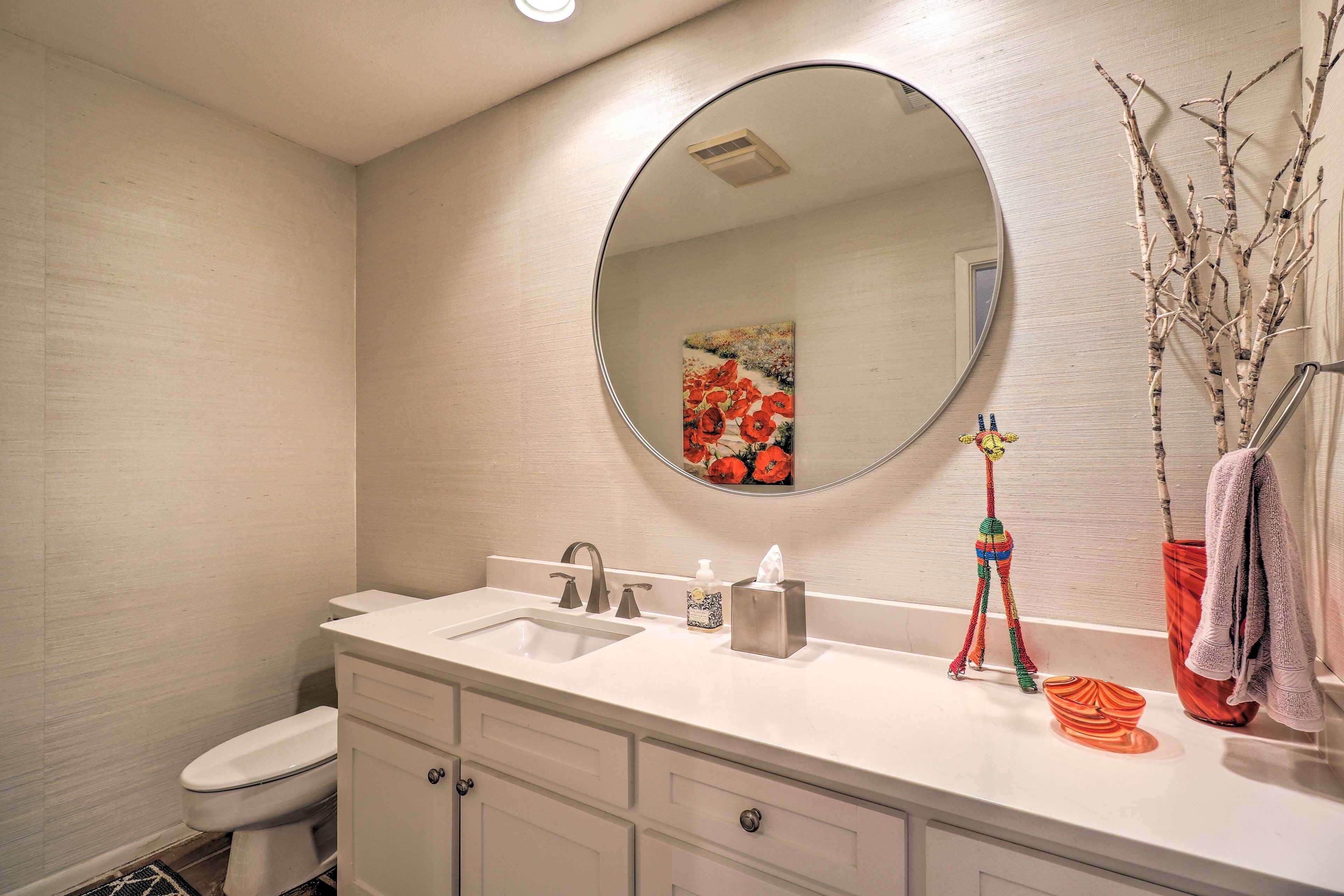 A bathroom with a white sink, a mirror, a toilet, and a decorative vase with branches.