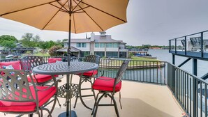 Une terrasse avec une table et des chaises, un grand parasol et une vue sur une maison et l’eau.