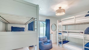 Een slaapkamer met een stapelbed, een blauwe stoel, een dressoir en een spiegel.