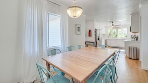 Een eetgedeelte met een houten tafel en blauwe stoelen, een kroonluchter en een keuken op de achtergrond.