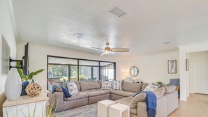 Een moderne woonkamer met een hoekbank, een plafondventilator en een groot raam met uitzicht op de omgeving.