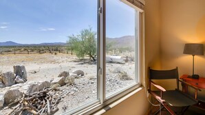 A room with a large window offering a view of a desert landscape with rocks, sparse vegetation, and distant mountains.