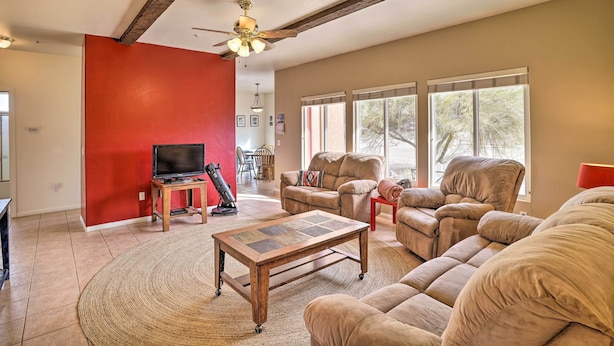 A spacious living room with a red accent wall, a ceiling fan, a large window with blinds, and a comfortable seating area.