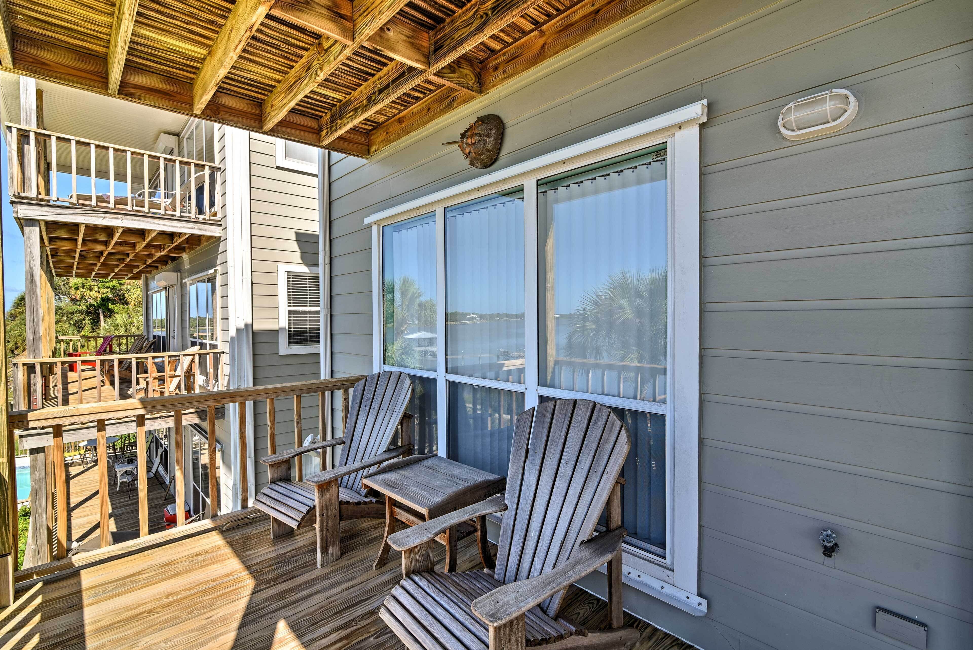 A wooden deck with Adirondack chairs and a table, overlooking a pool and a backyard.