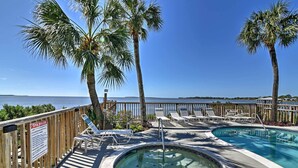 A pool area with lounge chairs, a hot tub, and a wooden fence. - Beachfront Cedar Key Condo w/ Pool, Spa & Views! (Cedar Key)