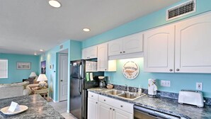 A modern kitchen with white cabinets, a stainless steel refrigerator, and a granite countertop. - Beachfront Cedar Key Condo w/ Pool, Spa & Views! (Cedar Key)