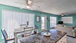 A spacious living room with a dining area, a ceiling fan, and a large window with blinds. - Beachfront Cedar Key Condo w/ Pool, Spa & Views! (Cedar Key)