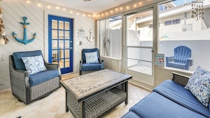 A sunlit patio with wicker furniture, a blue door, and nautical decor. - Indian Rocks Beach Home - 2 Blocks to Beach! (Indian Rocks Beach)