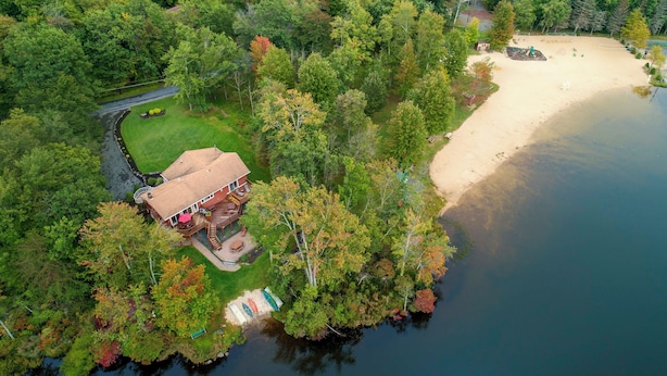 Vue aérienne d’une propriété au bord du lac, avec une maison, une plage de sable et un quai.