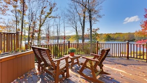 Une terrasse en bois avec une table et des chaises, donnant sur un lac aux couleurs automnales.