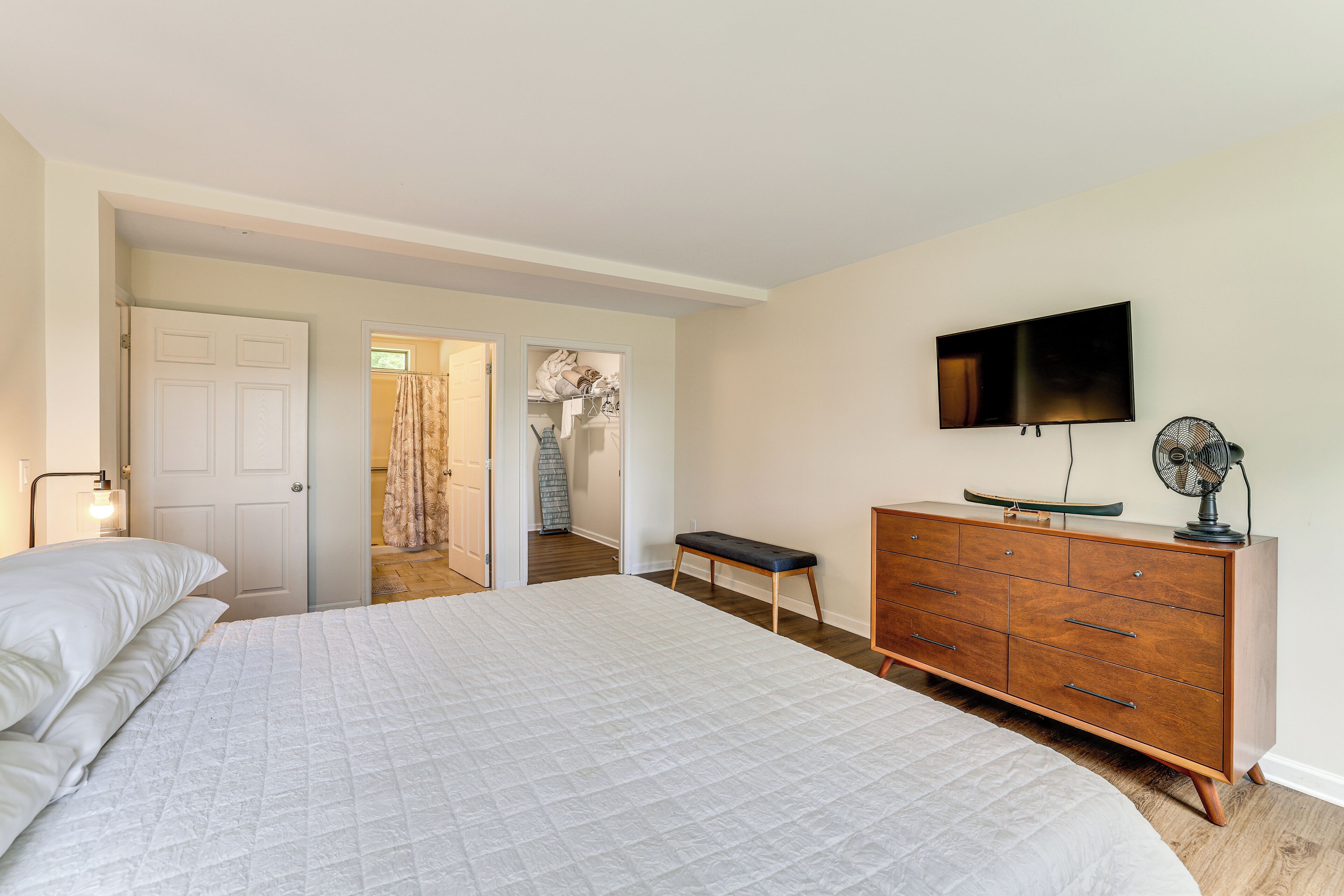 A bedroom with a large bed, a wooden dresser, a television, and a fan.