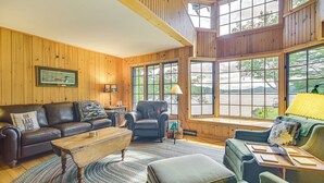 A cozy living room with wooden walls, a leather sofa, a green armchair, and a wooden coffee table.