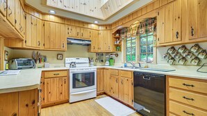 A kitchen with wooden cabinets, a stove, a dishwasher, and a window with a view of greenery.
