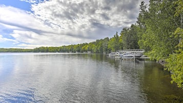 A calm lake with boats docked on the shore, surrounded by dense green trees.