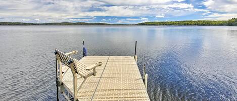 A wooden dock extending into calm water with a bench and a flagpole.