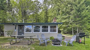 Uma cabana pequena com uma mesa de piquenique, duas cadeiras Adirondack, um braseiro e uma churrasqueira.