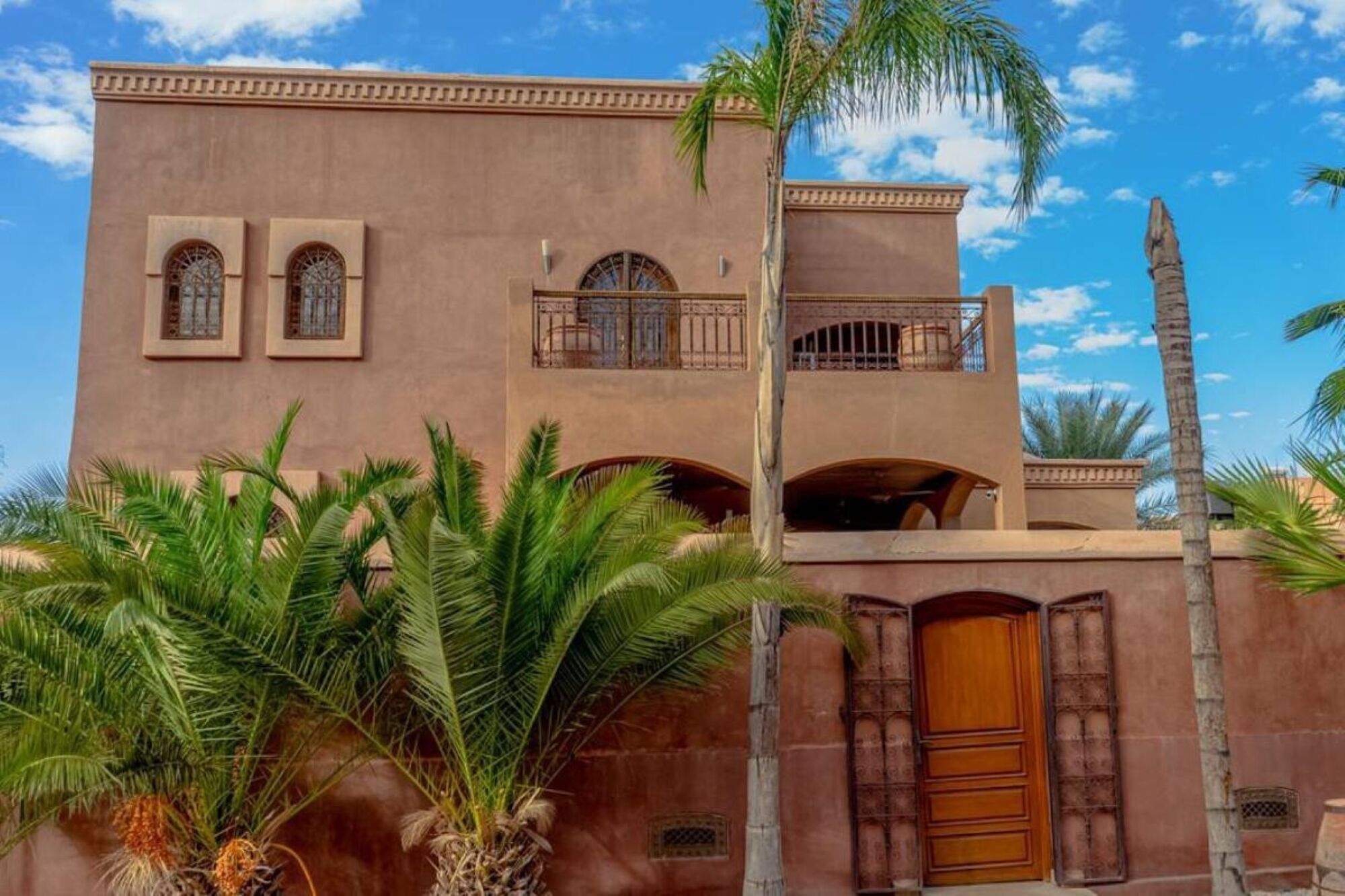 A two-story building with arched windows and balconies, surrounded by palm trees.