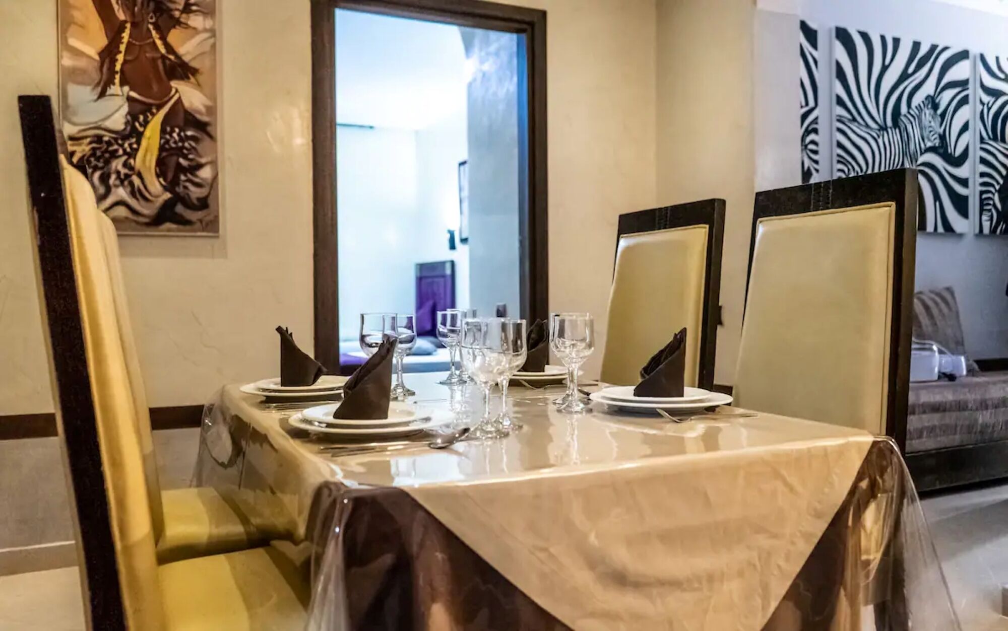 Una mesa de comedor con platos, vasos y servilletas, y un mural de cebra en la pared.