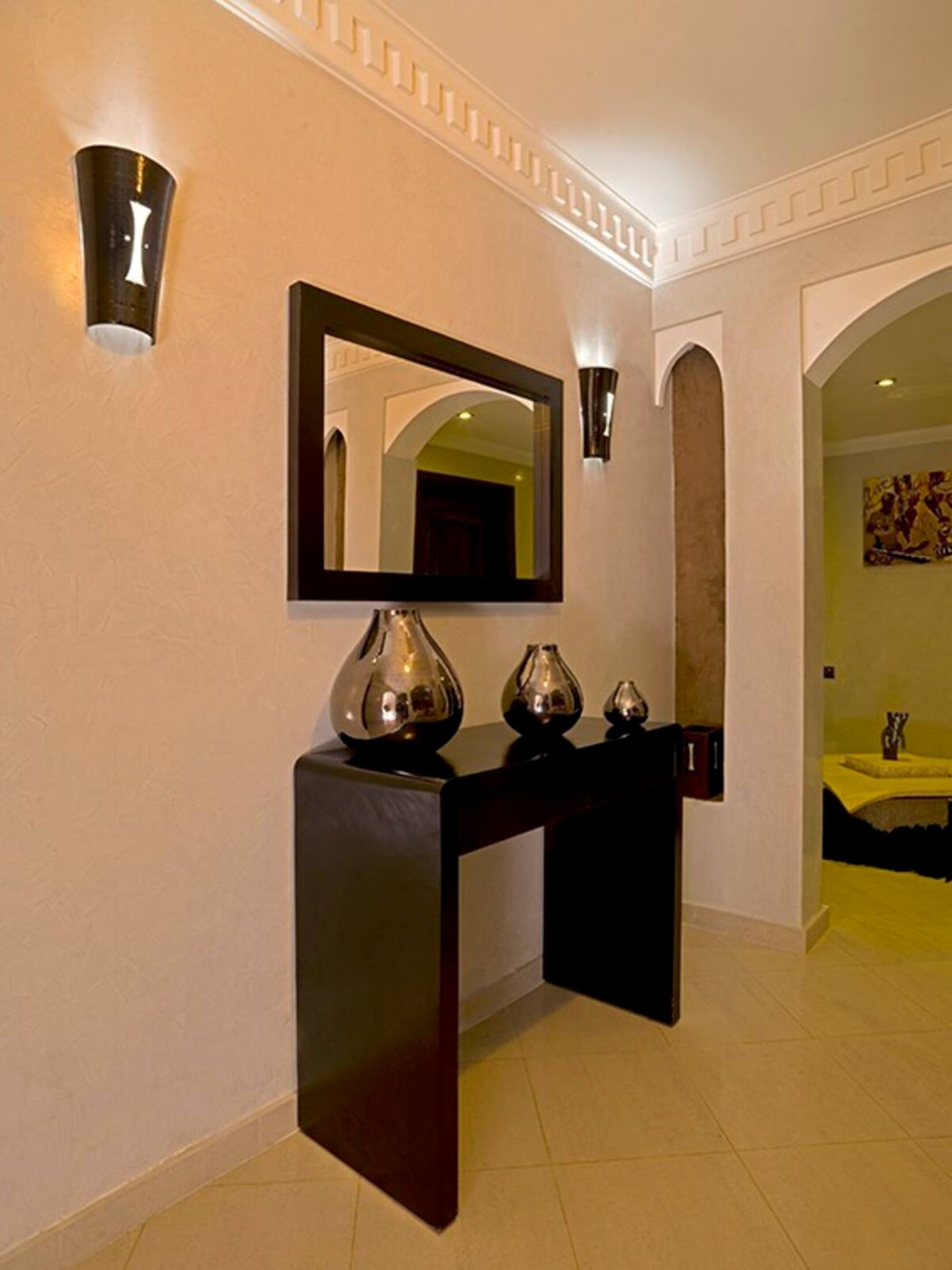 A hallway with a dark console table, a large mirror, and two wall-mounted sconces.