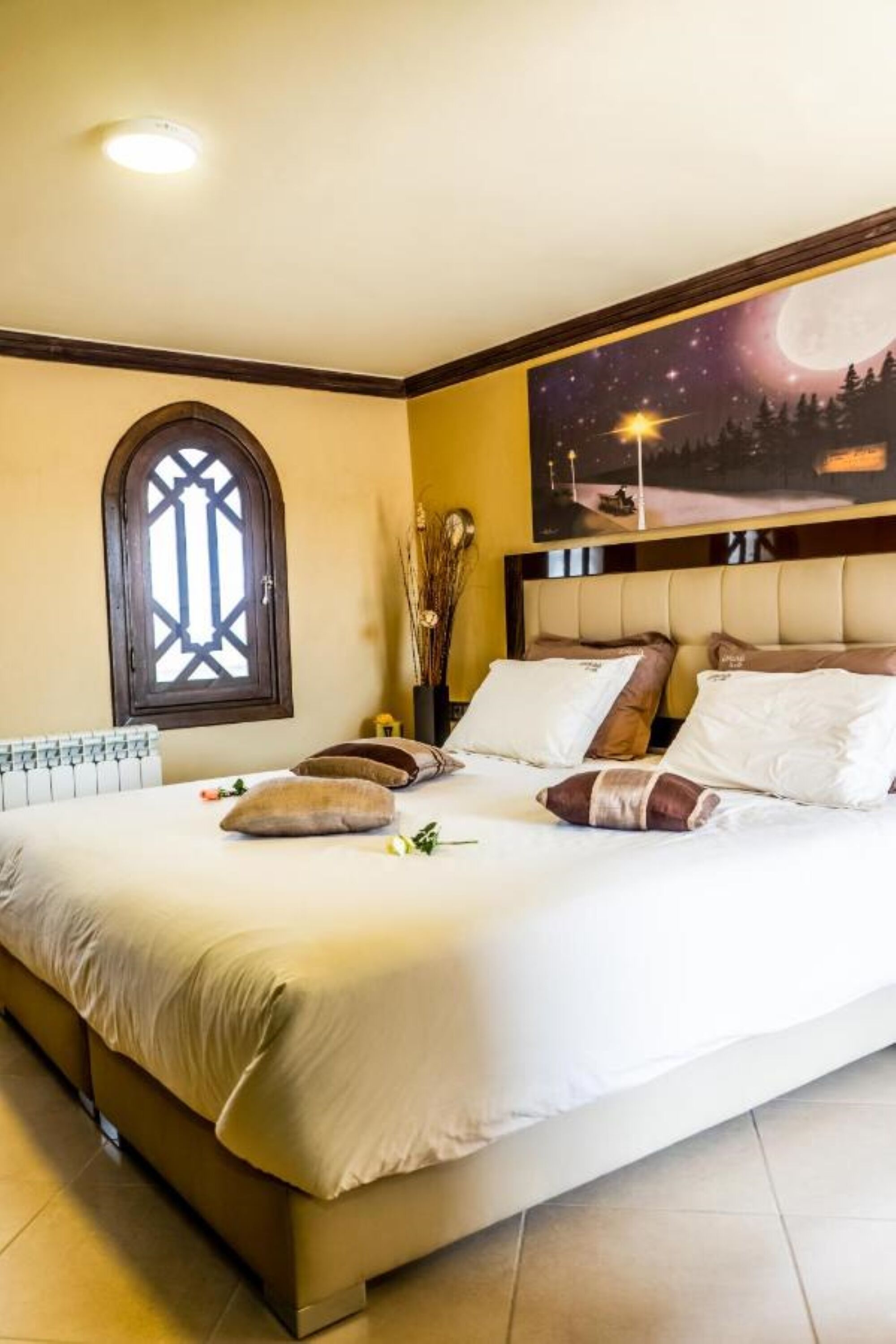 A bedroom with a large bed, a night sky mural, a window with a geometric design, and a night scene with trees and a moon.