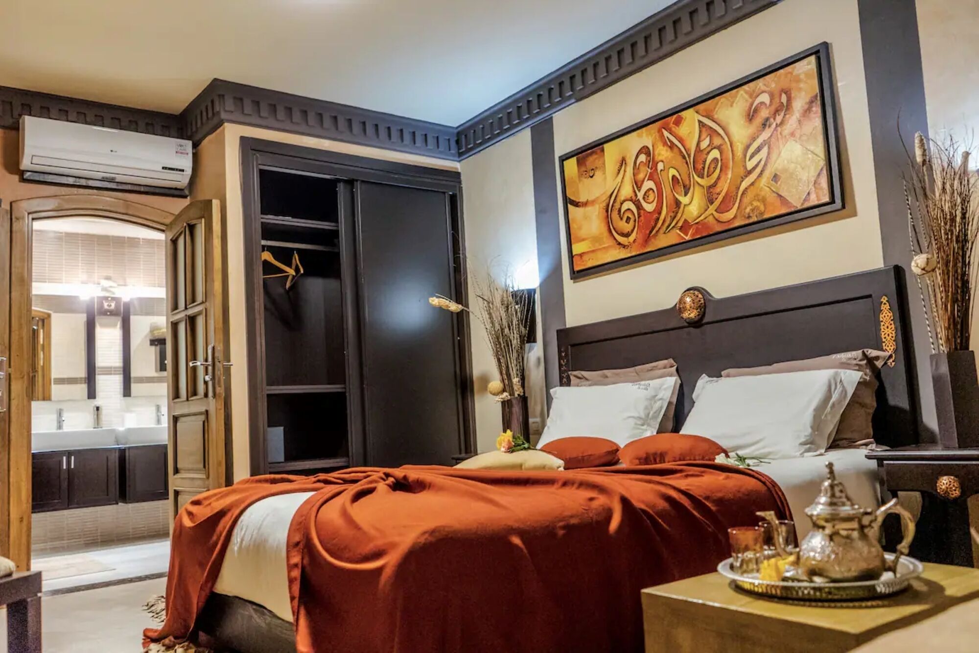 A hotel room with a large bed, a wardrobe, a bathroom with a mirror, and a decorative wall piece.