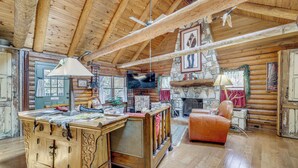 Een rustiek houten interieur met een houten plafond, een stenen openhaard, een televisie en een leren fauteuil.