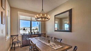 A dining area with a wooden table, six chairs, a chandelier, a large mirror, and a window with a snowy view. - Hike & Bike! Mtn-view Condo 1 Block to Main St (Winter Park)