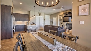 A modern kitchen with dark cabinets, a wooden dining table, and a chandelier. - Hike & Bike! Mtn-view Condo 1 Block to Main St (Winter Park)