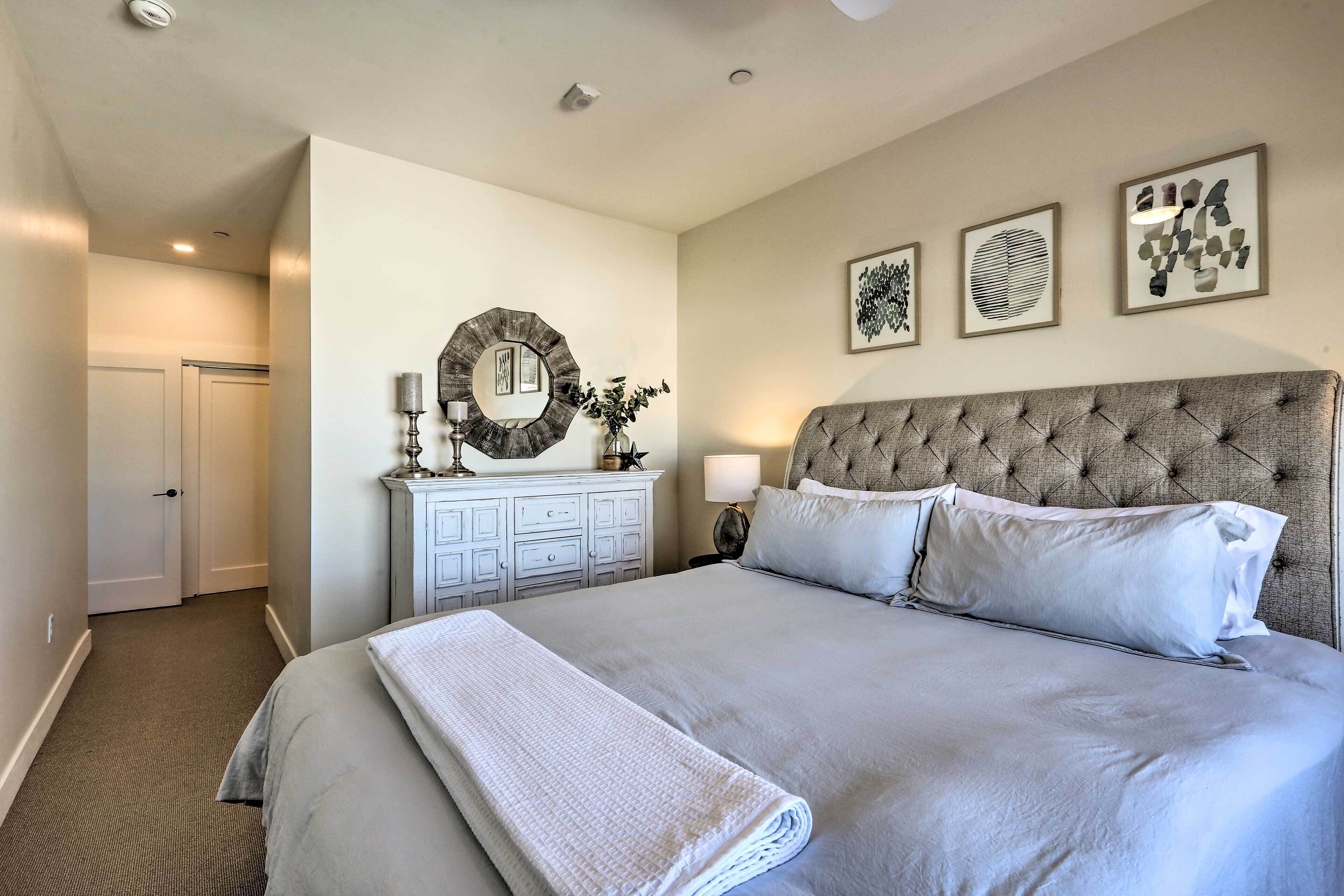 A neatly arranged bedroom with a large bed, a dresser, a mirror, and framed artwork on the wall.