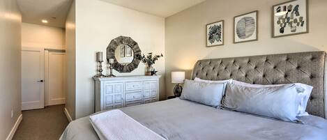 A neatly arranged bedroom with a large bed, a dresser, a mirror, and framed artwork on the wall.