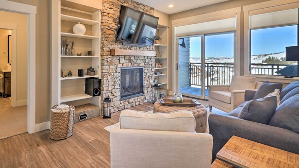 A modern living room with a stone fireplace, a flat-screen TV, and a balcony with a view. - Hike & Bike! Mtn-view Condo 1 Block to Main St (Winter Park)