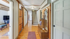 Un pasillo con pisos de madera, un banco, una escalera y una puerta con perchero.