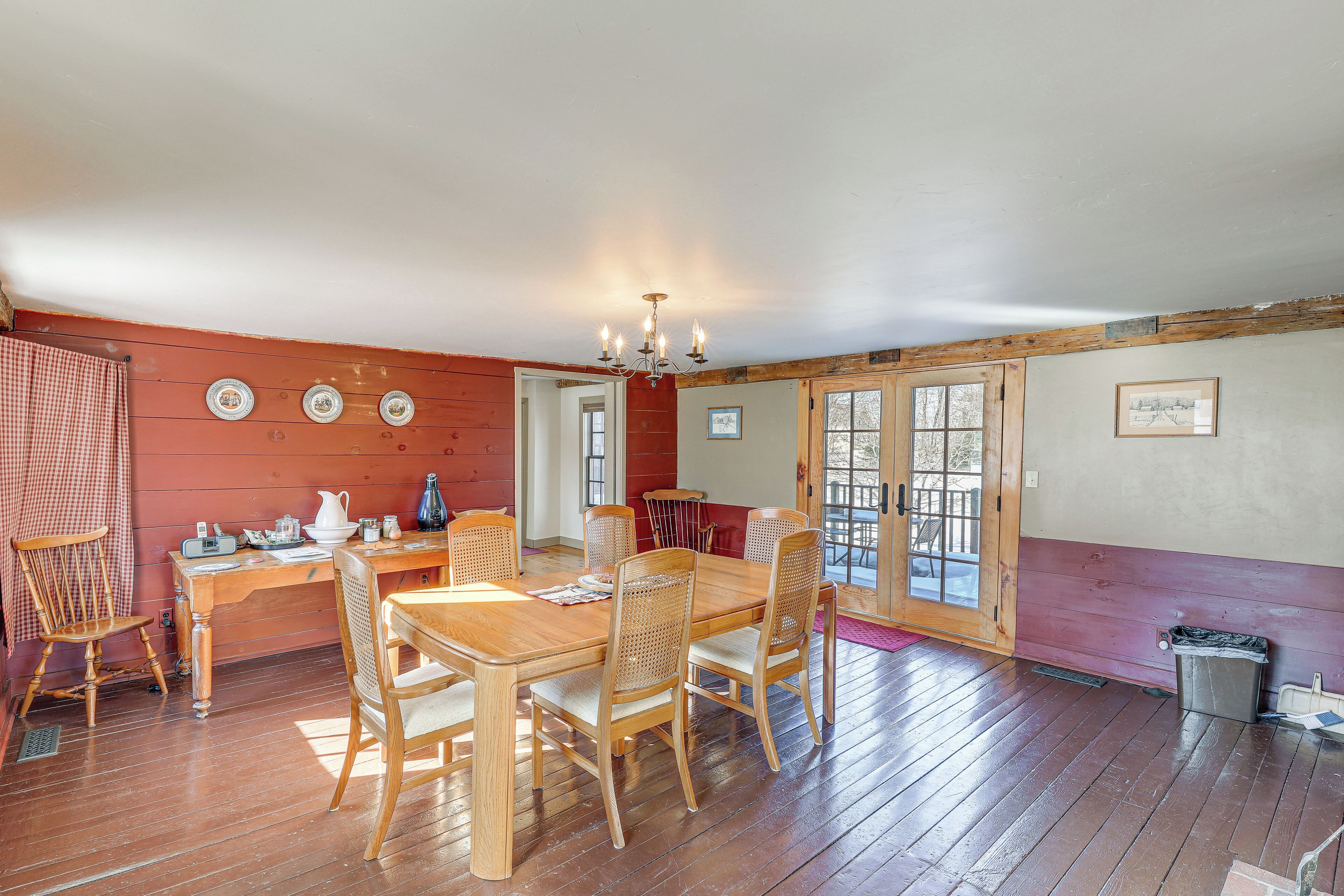 A dining area with a wooden table and chairs, a chandelier, and a view through a door to the outside.