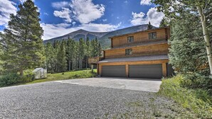 A two-story log cabin with a garage, surrounded by a gravel driveway and dense forest. - Silver Plume Mountain Haven With Views & Deck! (Silver Plume)