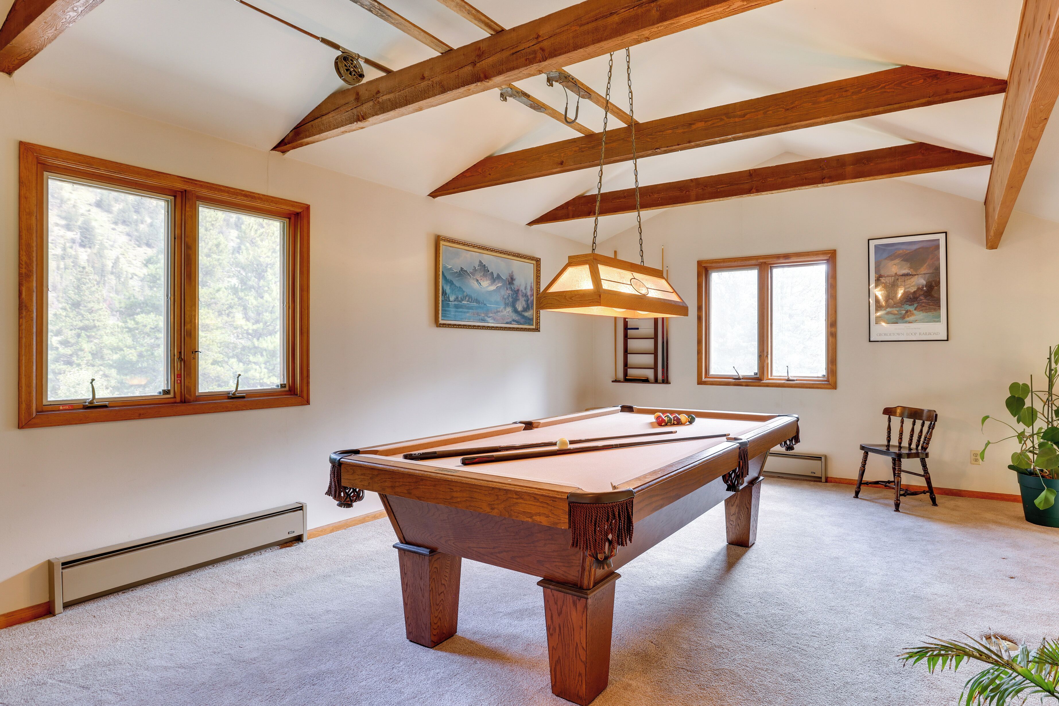 A pool table in a room with wooden beams, large windows, and a ceiling fan.
